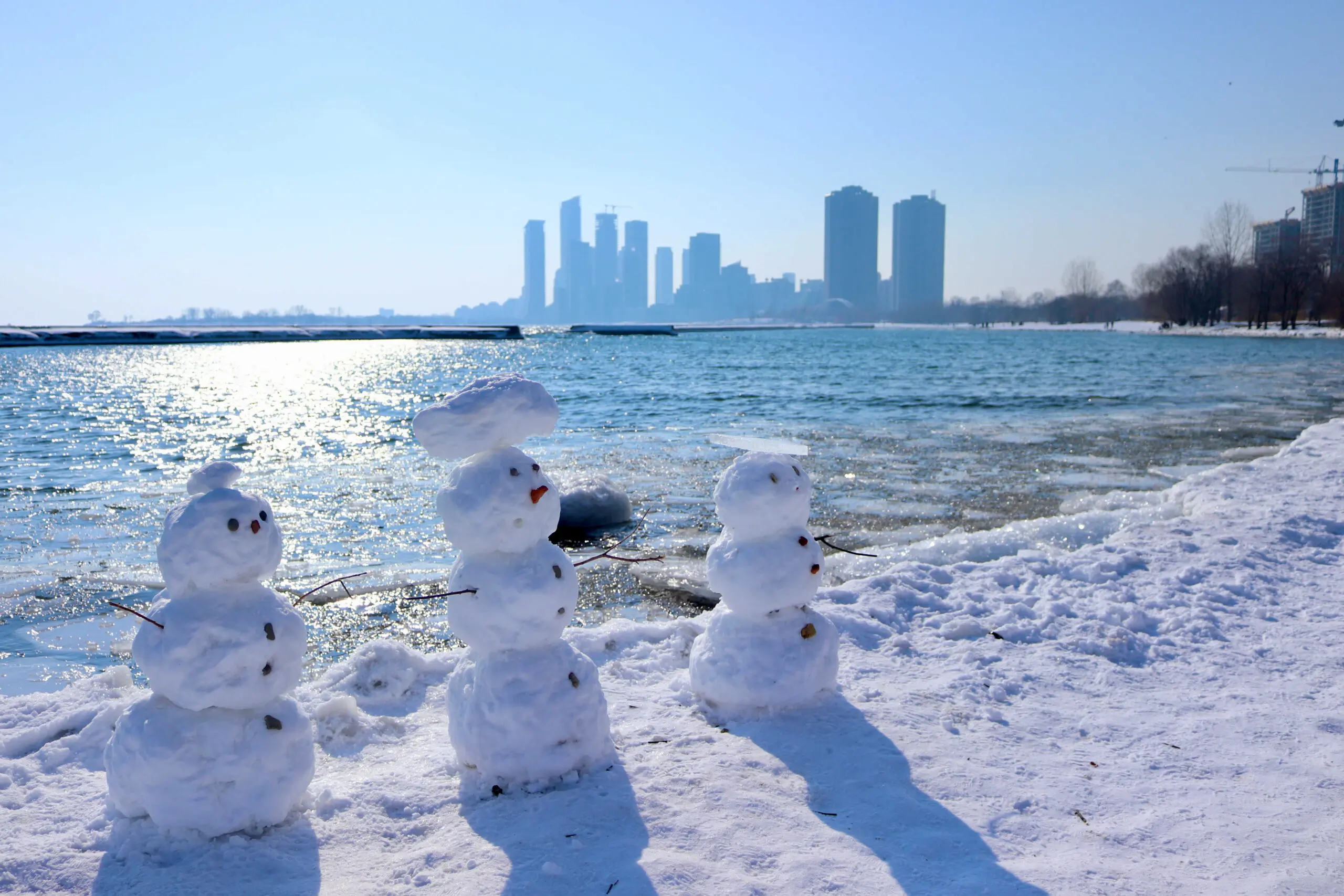 Three snow men with buildings on the background across the lake, Humber Bay. Biking around Lake Ontario. Love-hate relationship.